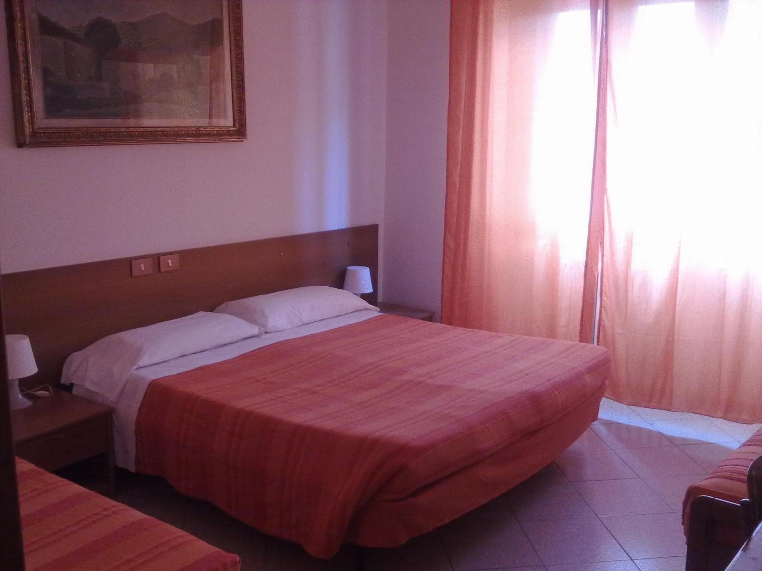 A hotel room with a large bed, a nightstand, a lamp, and a painting on the wall.
