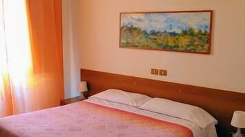 A hotel room with a bed, a nightstand, a lamp, a painting on the wall, and a window with curtains.