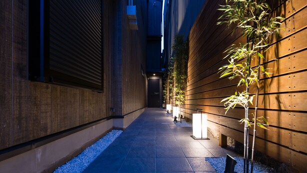 A narrow pathway with tiled flooring, a wooden wall on one side, and a small tree on the other. - Villa Front Kyoto Seimei (Kyoto)