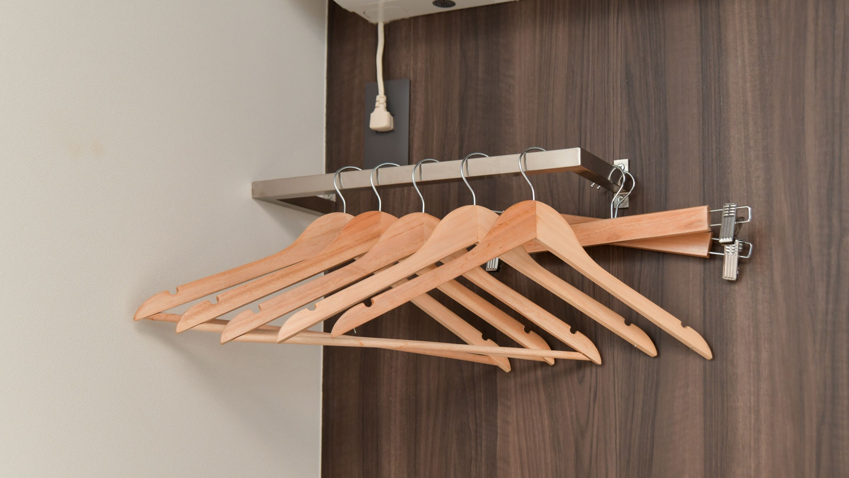 A wooden clothes rack with multiple hangers against a dark wooden wall.