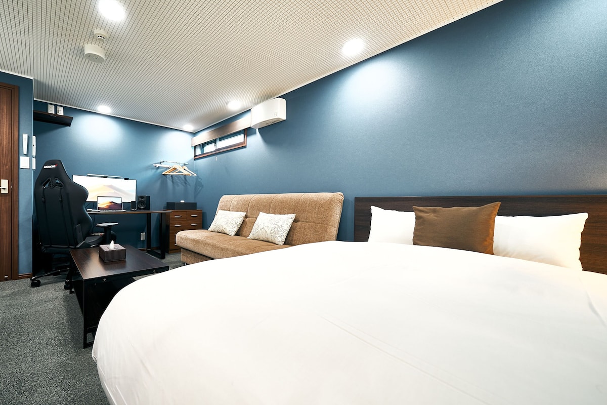 A hotel room with a large bed, a sofa, a desk with a computer, and a wardrobe.
