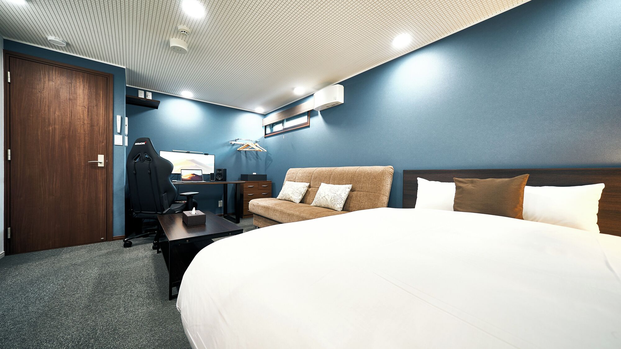A hotel room with a large bed, a desk with a computer, a chair, and a wardrobe.