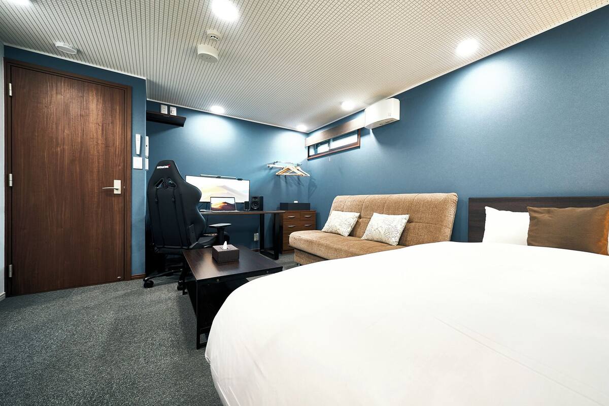 A hotel room with a large bed, a desk with a computer, a chair, and a wardrobe.