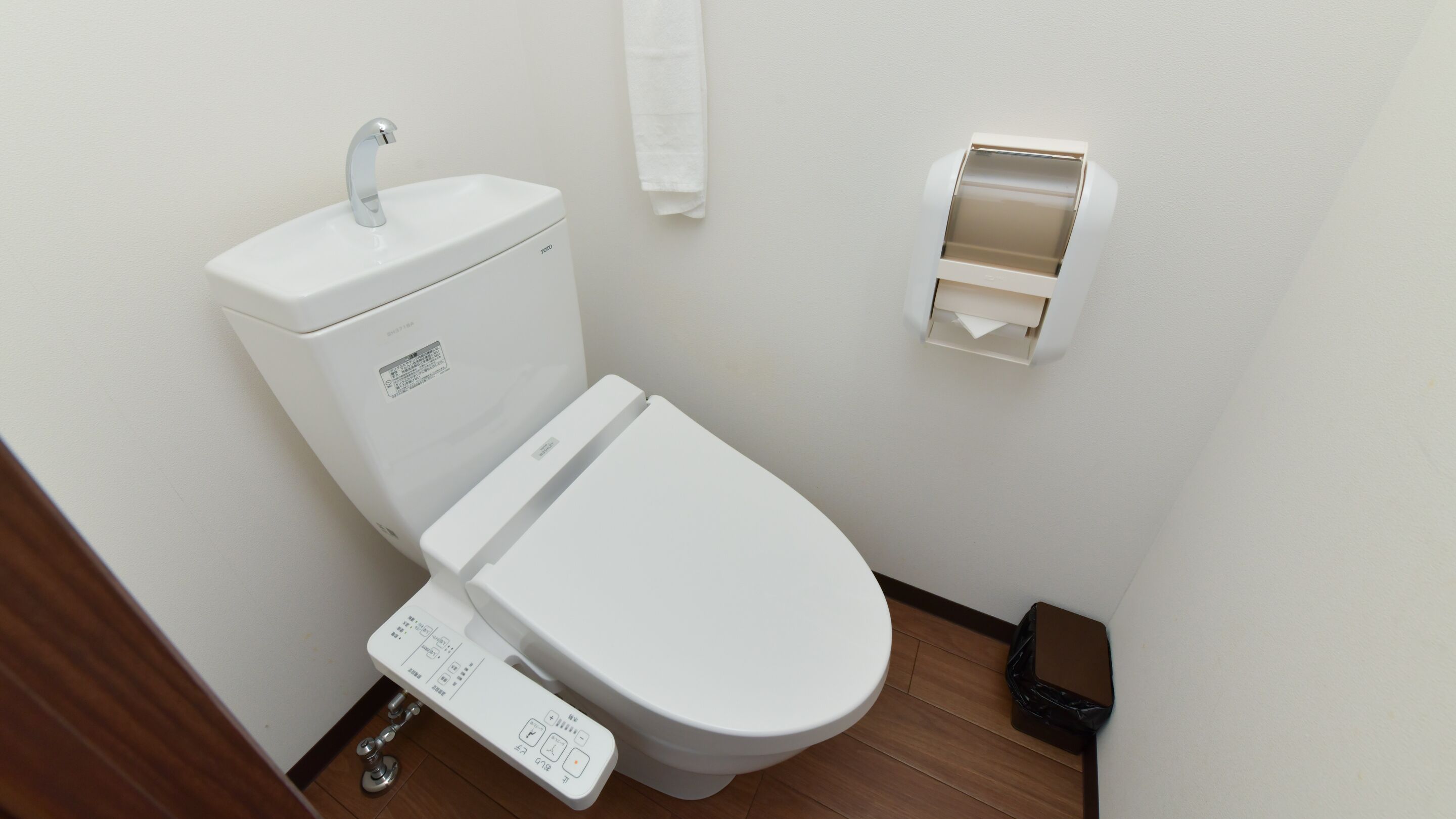 Un inodoro blanco con un panel de control, un dispensador de toallas de papel y un cubo de basura.