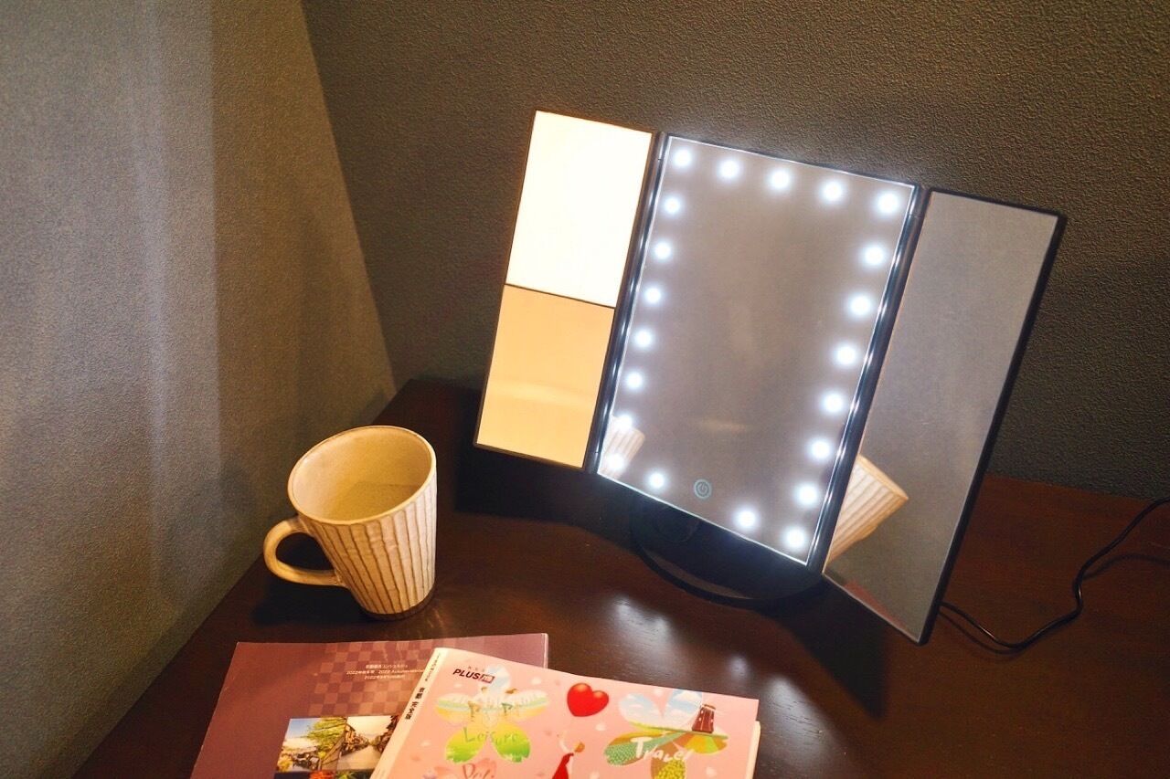 A vanity mirror with lights, a mug, and a magazine on a wooden table.