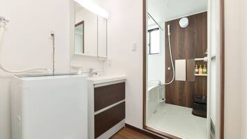 Un baño moderno con cabina de ducha de vidrio, lavabo empotrado y lavadora.