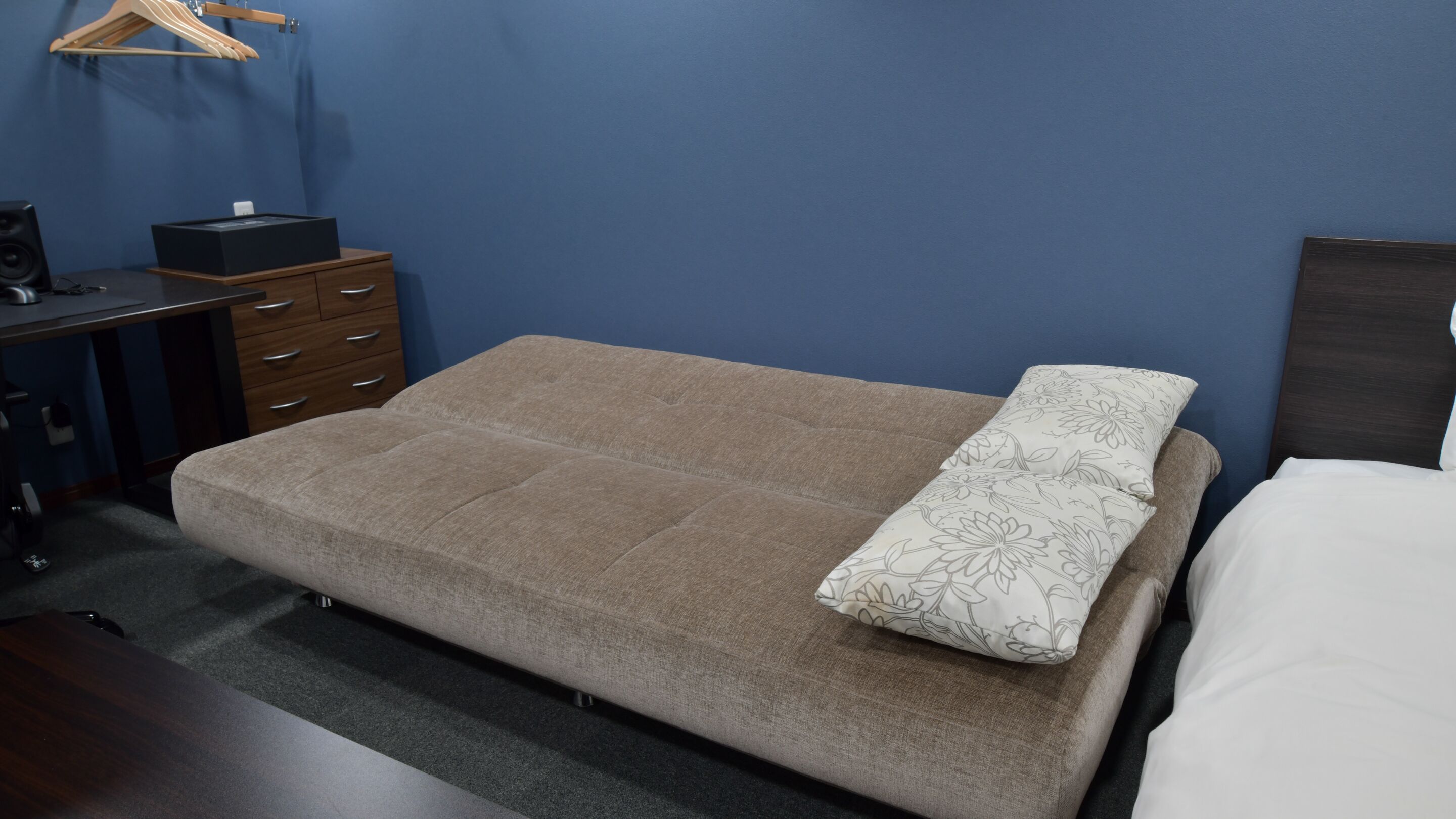 A bedroom with a bed, a dresser, a desk, and a hanging clothes rack.