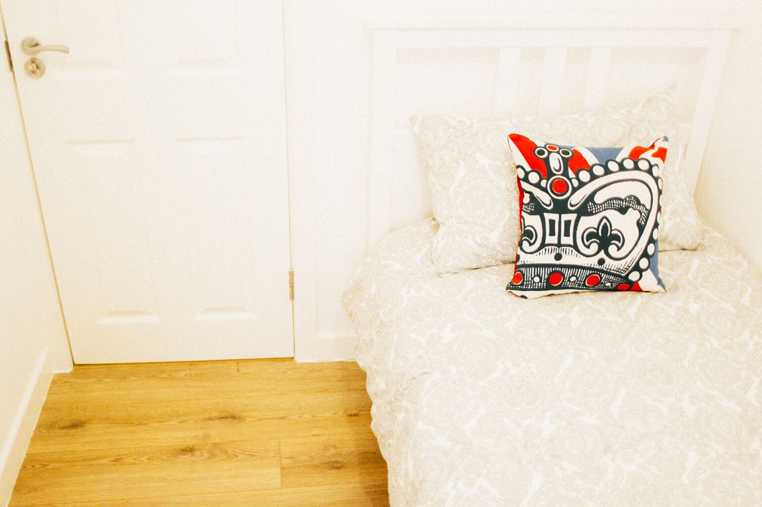 A bedroom with a white bed, a decorative pillow, and a wooden floor.