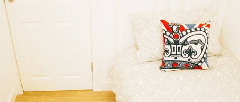 A bedroom with a white bed, a decorative pillow, and a wooden floor.