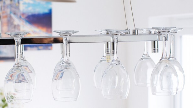 A row of empty wine glasses hanging from a metal bar.