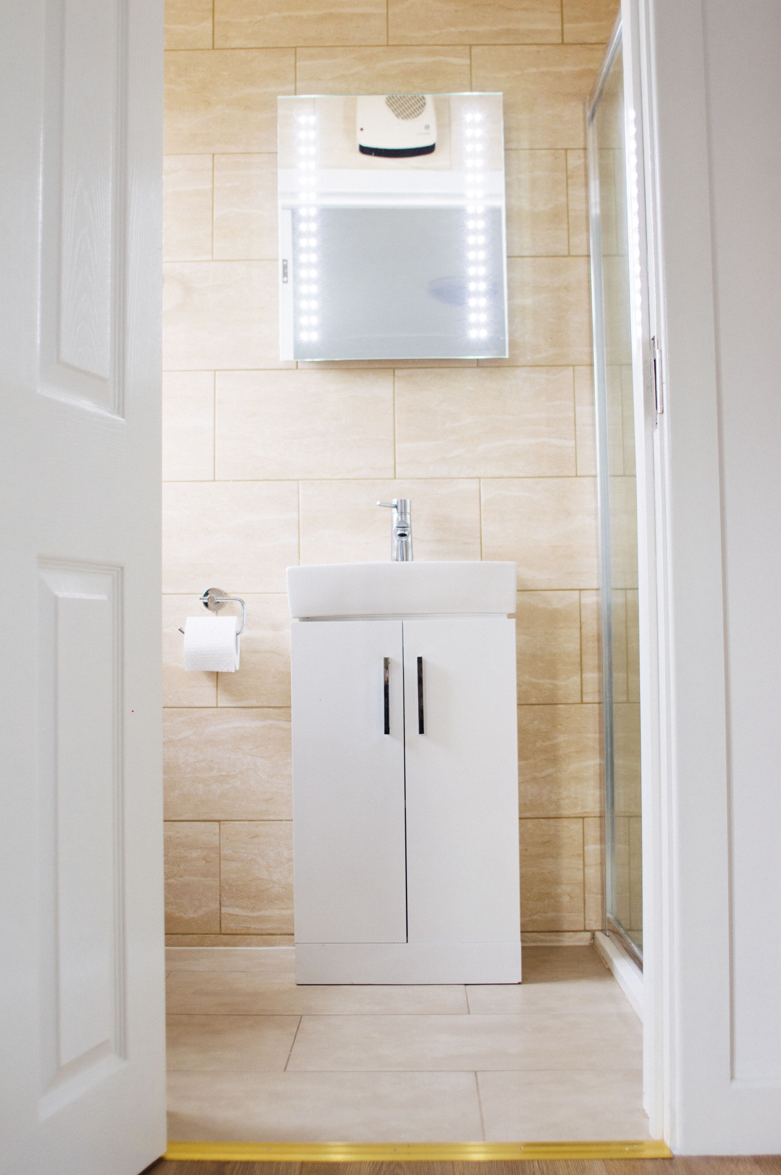 A bathroom with a white sink, a mirror, and a toilet paper holder on the wall.