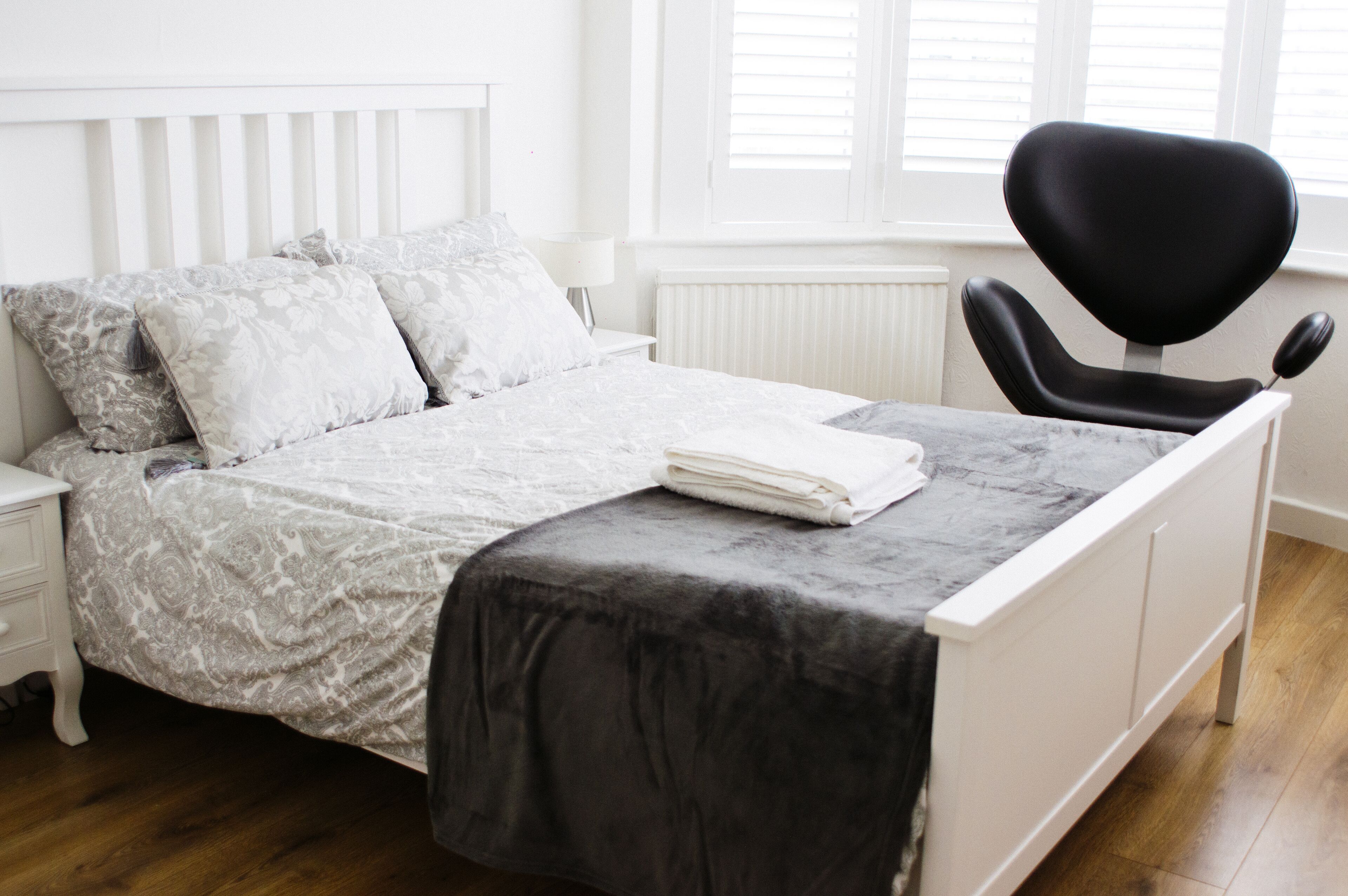 A neatly made bed with a patterned bedspread, a black chair, and a white nightstand with a lamp.
