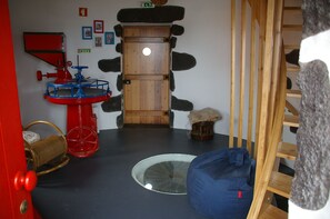Una habitació amb una porta de fusta, una màquina vermella i blava, un seient informal blau i un tamboret de fusta petit.