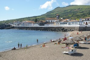 A coastal town with a beach, buildings, and a hill in the background.