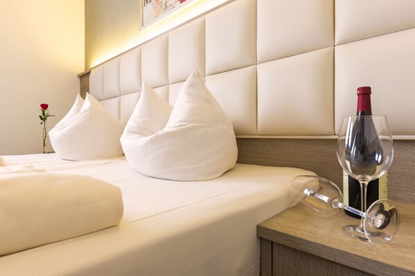 A neatly made bed with white pillows and a wine bottle and glass on a wooden bedside table. - Bavaria Hotel Superior (Stuttgart)