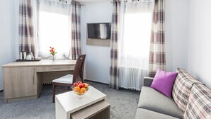 A modern room with a desk, a television mounted on the wall, a sofa, and a small table with a fruit bowl. - Bavaria Hotel Superior (Stuttgart)