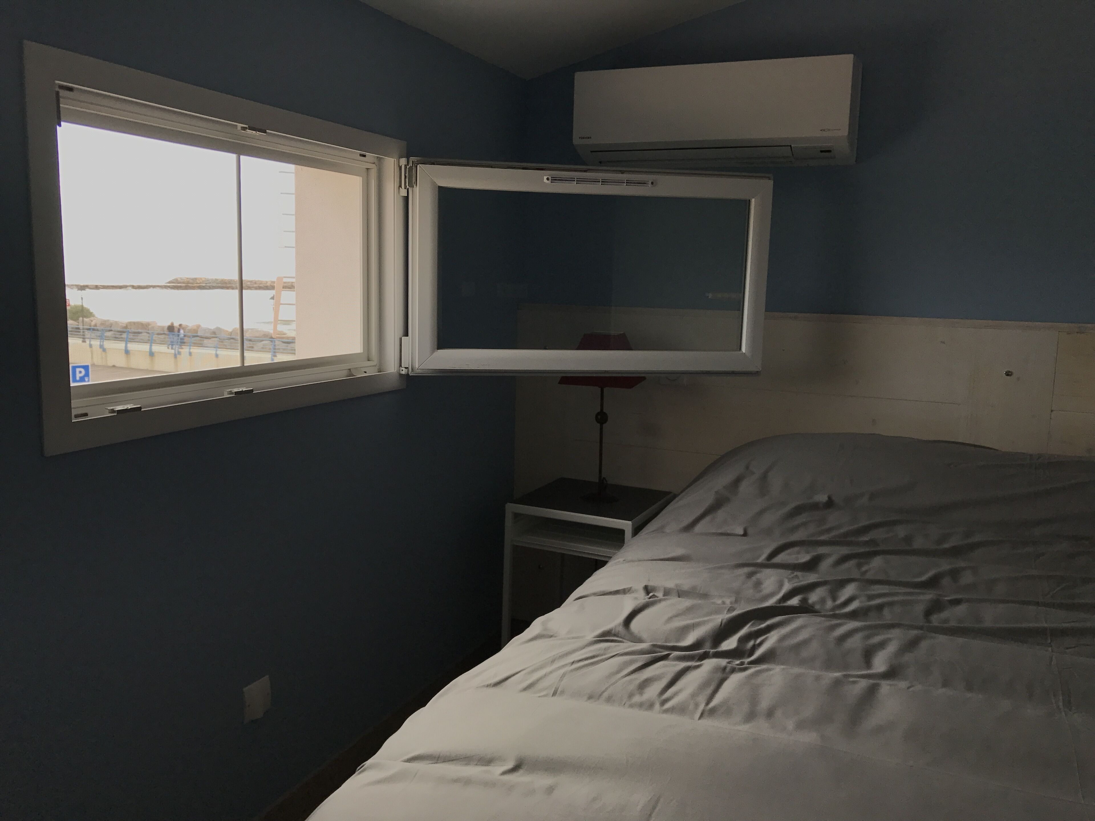 A bedroom with a bed, a window, a nightstand, and an air conditioning unit.
