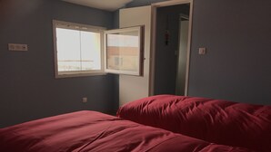 A bedroom with a single bed, a window, and a door leading to another room. - Luxury seafront apartment 4**** First floor (Saintes-Maries-De-La-Mer)