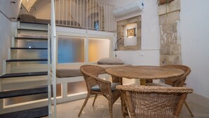 Un dormitorio con literas, una mesa redonda de madera, sillas de mimbre y una pared de piedra.