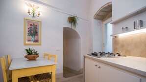 Una cocina compacta con una mesa de comedor, sillas, estufa a gas y una planta colgante.