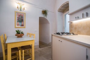 Cozinha compacta com mesa, cadeiras, fogão a gás e uma planta pendurada.