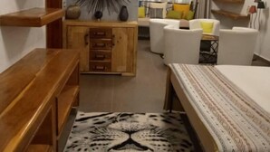 A bedroom with a bed, a wooden dresser, a mirror, and a patterned rug. - Le Calao du Lac Rose (Niaga)
