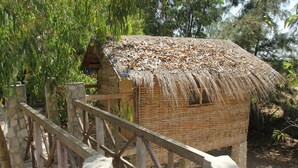 A rustic thatched-roof hut with a wooden fence in front, surrounded by greenery. - Le Calao du Lac Rose (Niaga)