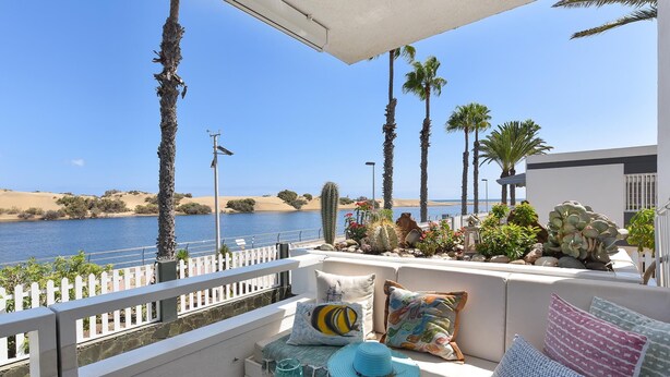 Un balcón con vistas al mar, amueblado con un sofá, cojines y una mesa con bebidas y frutas.