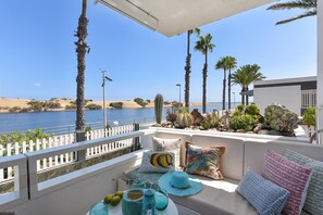A balcony with a view of the sea, furnished with a sofa, cushions, and a table with drinks and fruits. - Maspalomas Charca AB by VillaGranCanaria (San Bartolomé de Tirajana)