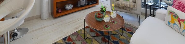 A living room with a round wooden coffee table, a colorful rug, a white sofa, and a bookshelf with decorative items. - Maspalomas Charca AB by VillaGranCanaria (San Bartolomé de Tirajana)