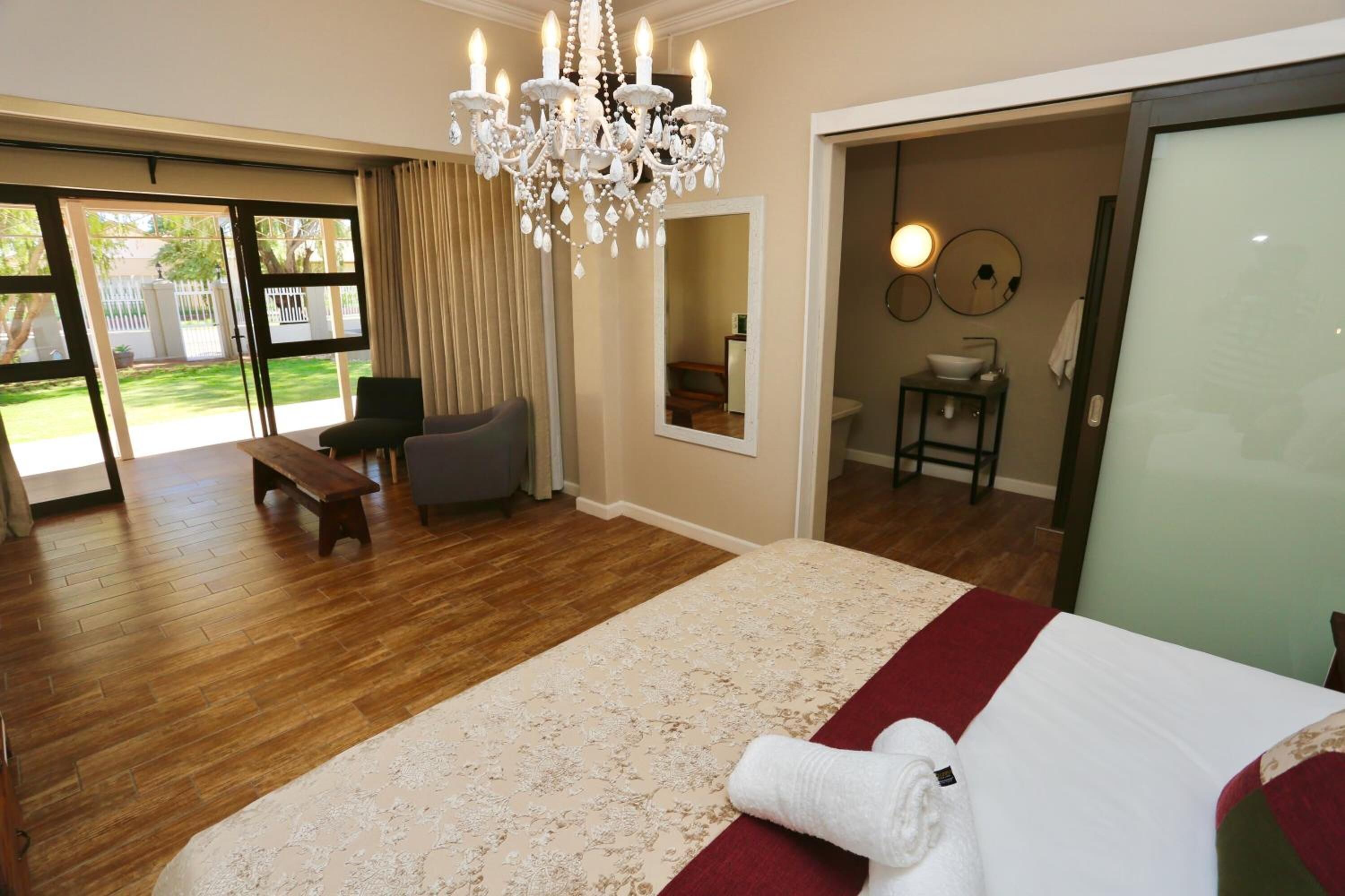 A bedroom with a large bed, a chandelier, a bench, a small table, and a bathroom visible through an open door.