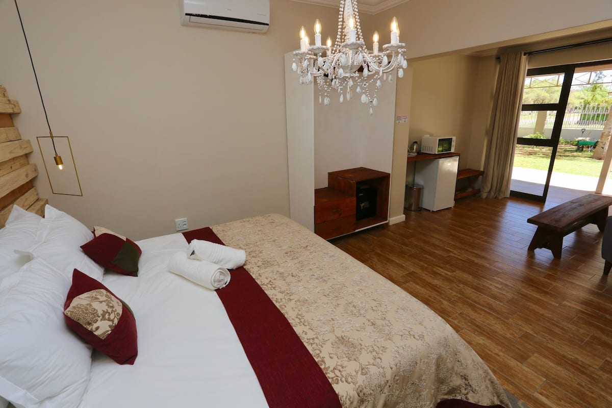 Une chambre spacieuse avec un grand lit, un lustre, un plancher en bois et une porte-fenêtre coulissante donnant sur un espace extérieur.