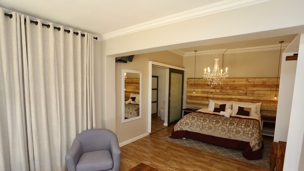Une chambre à coucher avec un grand lit, une tête de lit en bois, un lustre et un fauteuil gris.