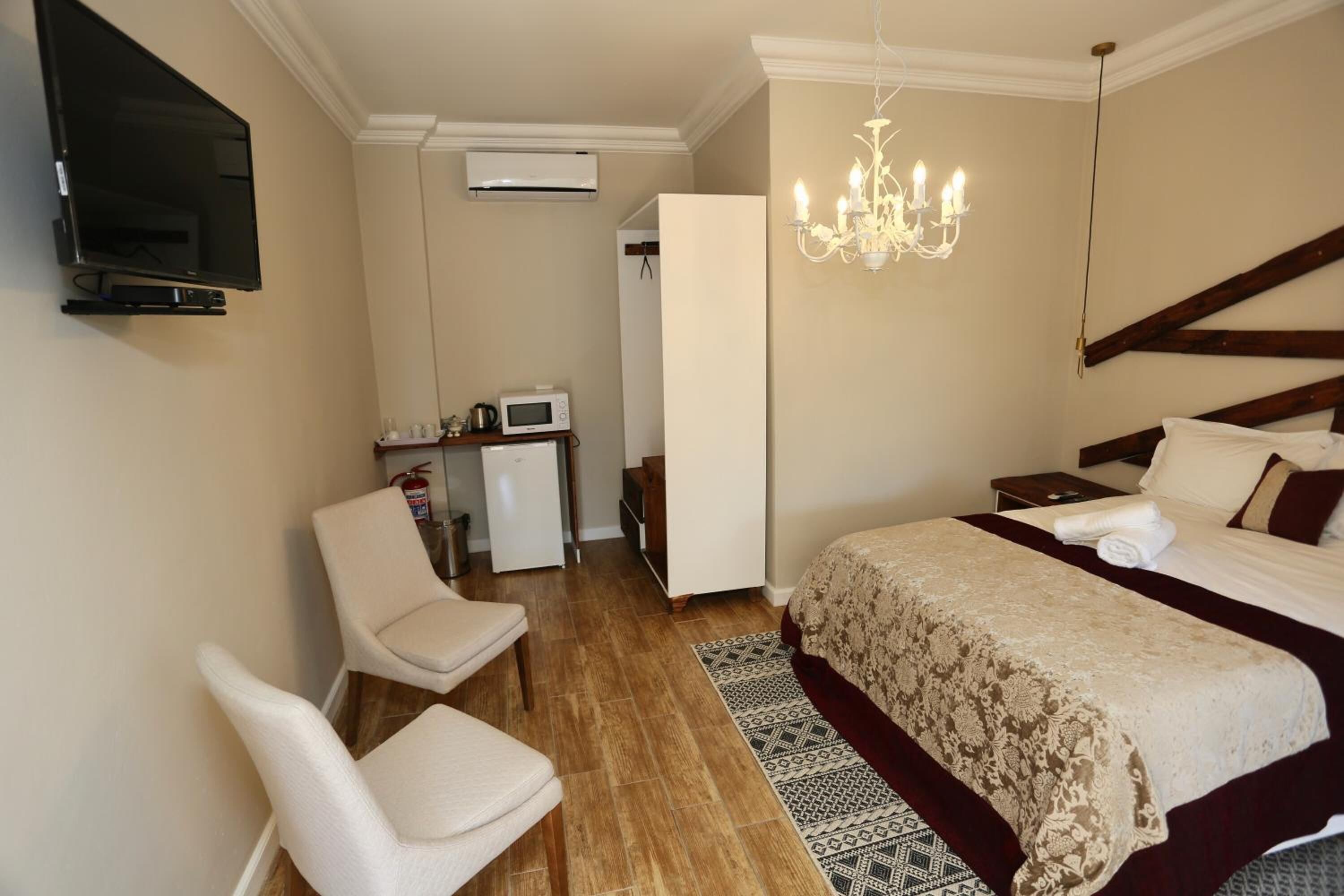 Ett hotellrum med en säng, en TV, ett skrivbord med en mikrovågsugn, en stol och en kristallkrona.