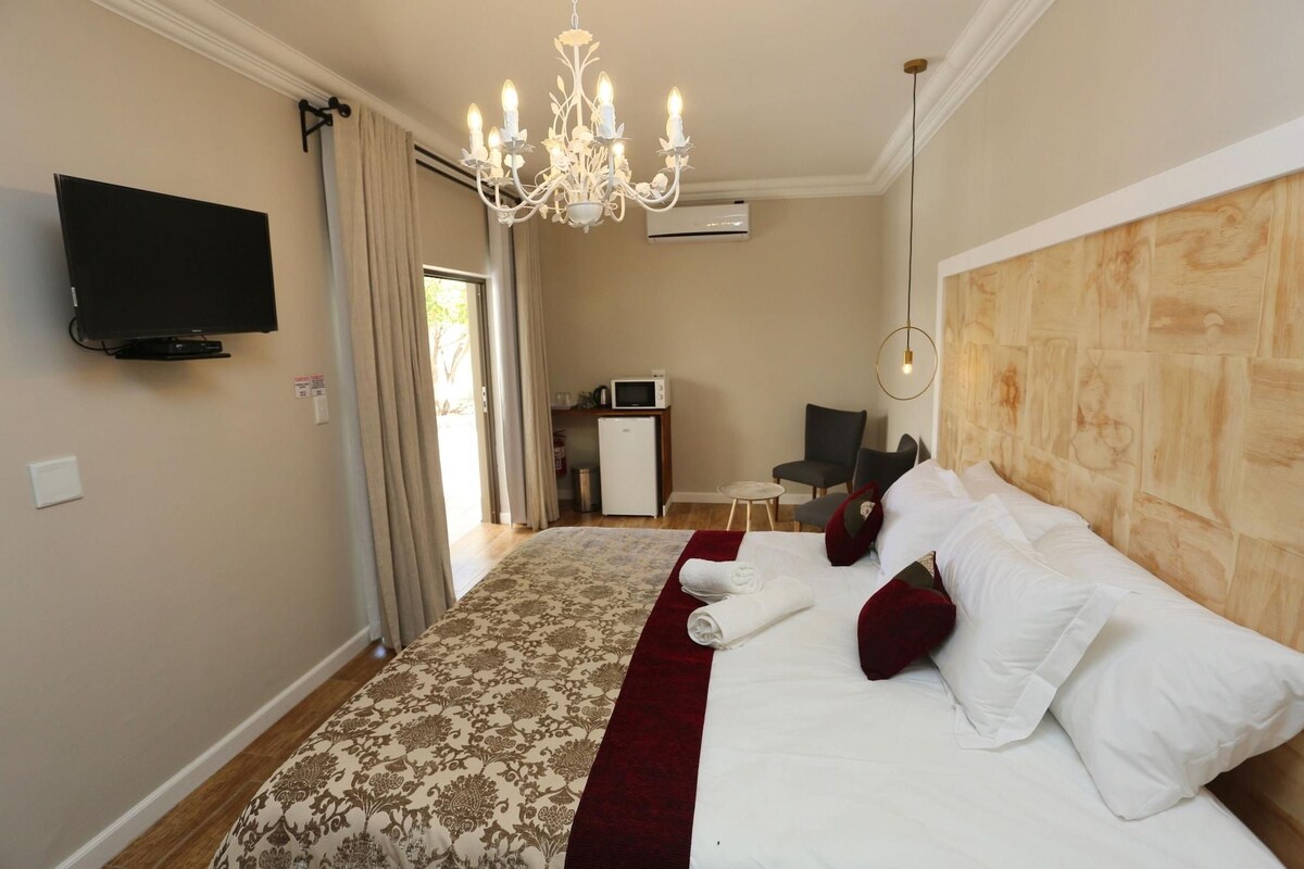 Ein Hotelzimmer mit einem großen Bett, einem Flachbildfernseher, einer Kristallleuchtre, einem Holz-Kopfschild und einem kleinen Tisch mit Stuhl.
