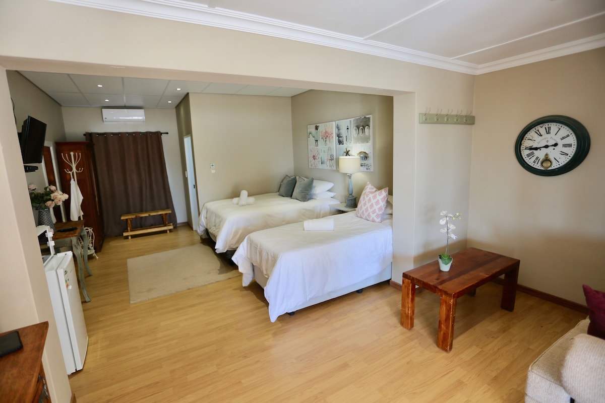 Une chambre d’hôtel avec deux lits, une table en bois, une horloge et une lampe fixée au mur.