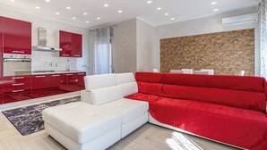A modern living room with a white sofa and red cushions, a kitchen with red cabinets, and a stone wall. - Villa Joel with splendid swimming pool in the heart of Fontane Bianche (Fontane Bianche)