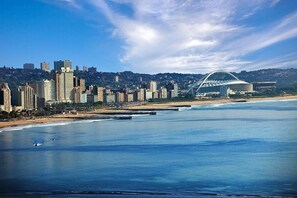 A coastal cityscape with high-rise buildings, a beach, and a distinctive stadium-like structure. - Cybele Lodge (Kloof)