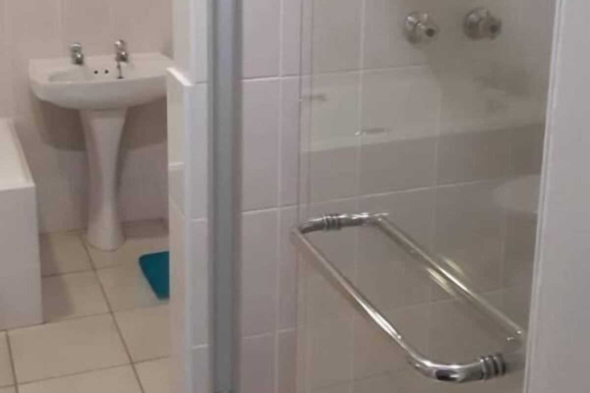Un baño con ducha de vidrio, lavamanos pedestal y una decoración de corazón en la pared.