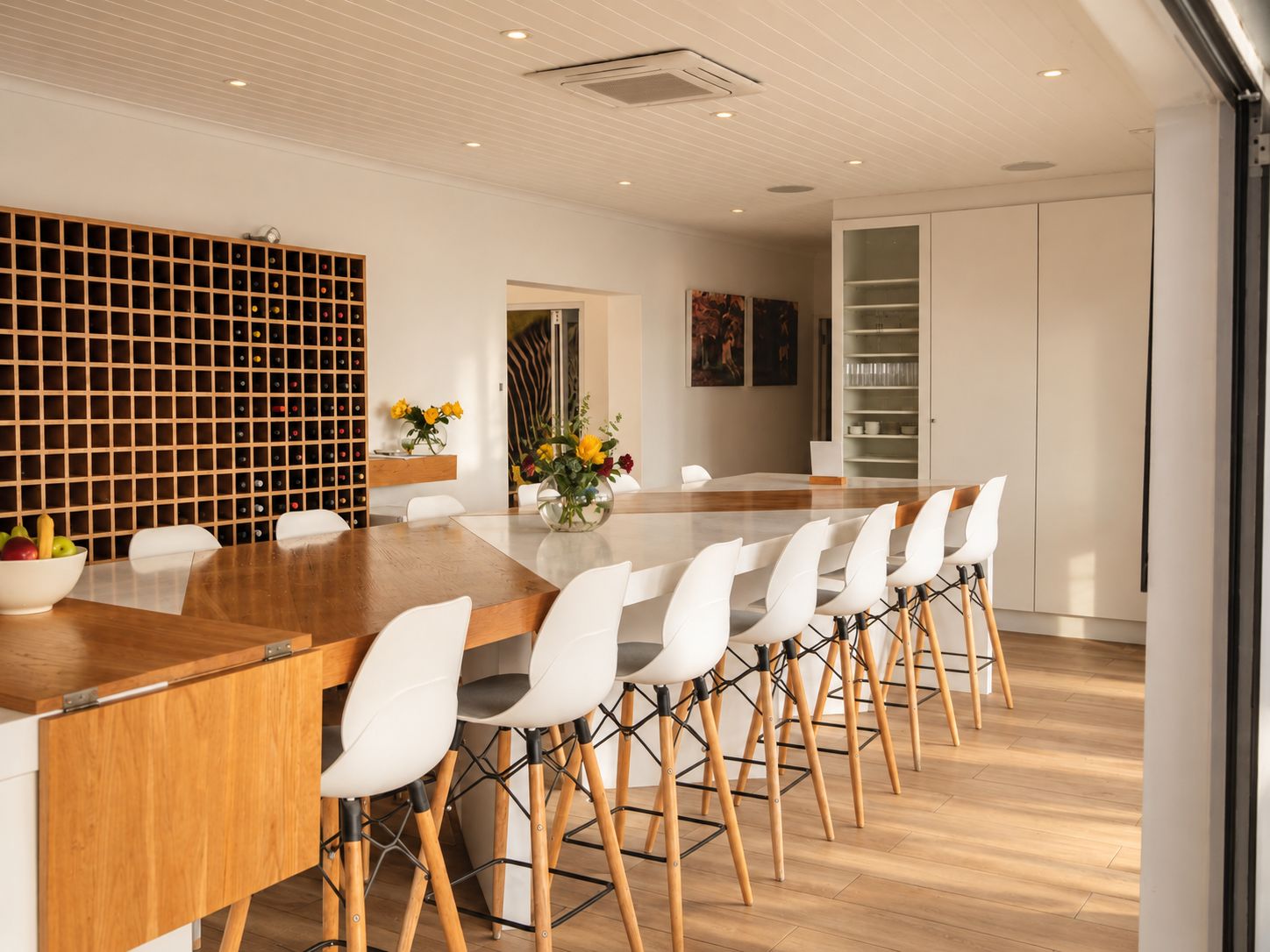 A modern dining area with a wooden table, white chairs, and a wine rack.