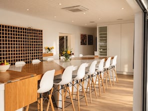 Un comedor moderno con una mesa de madera, sillas blancas y una estantería para vinos.