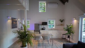 A modern kitchen with white cabinets, a dining area with a table and chairs, and a living room with a sofa. There are potted plants and a TV in the kitchen. - theLAB Franschhoek (Franschhoek)