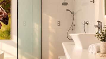 A modern bathroom with a glass shower enclosure, a white bathtub, and a sink with a plant.
