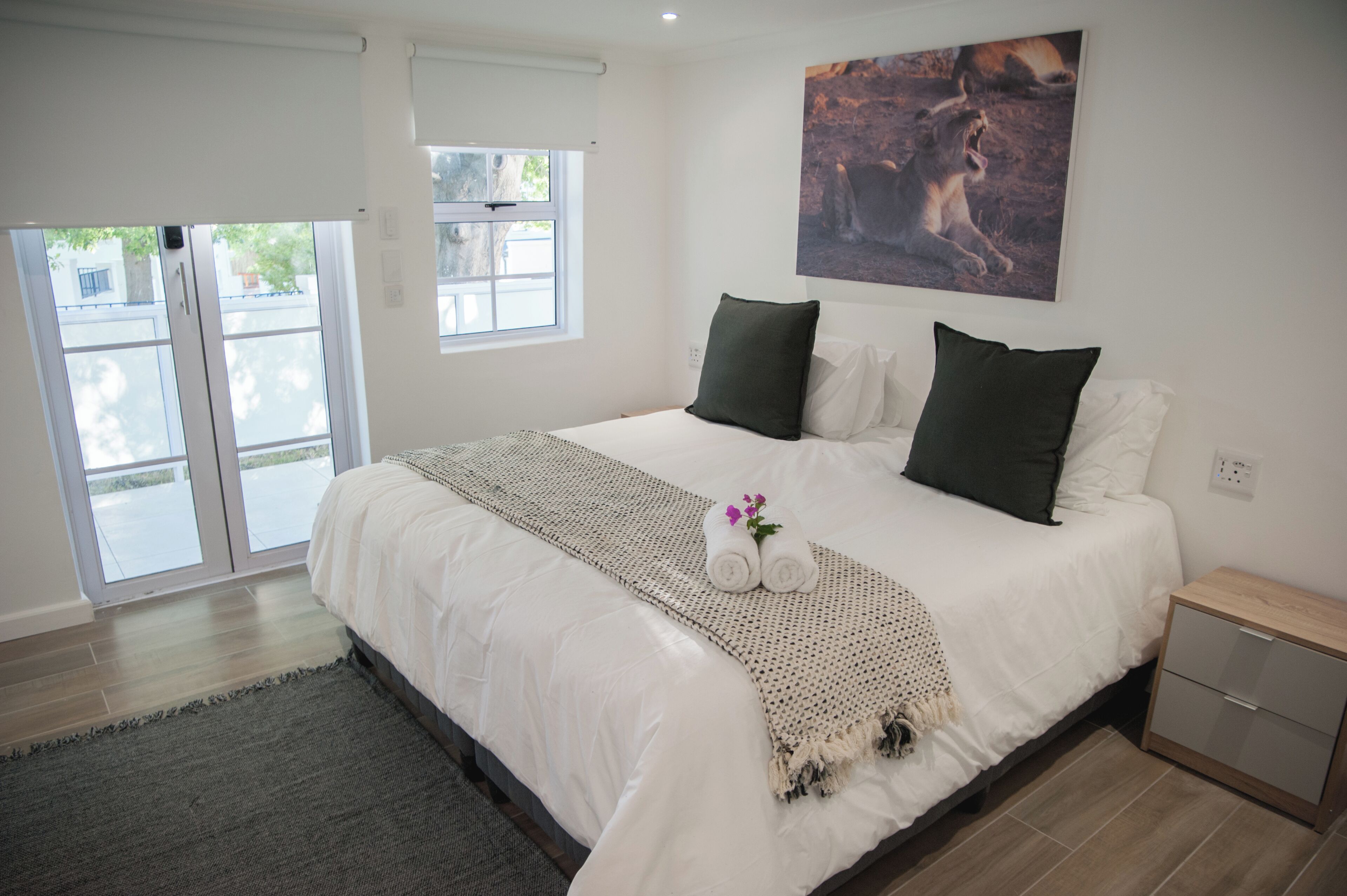 A bedroom with a large bed, a window, a painting, and a nightstand.