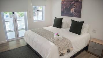 A bedroom with a large bed, a window, a painting, and a nightstand.