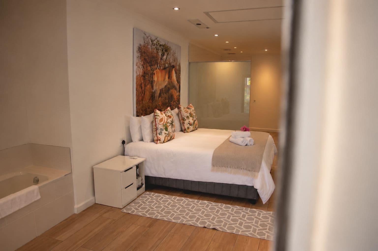 A modern bedroom with a large bed, a bedside table, a built-in bench, and a large window.