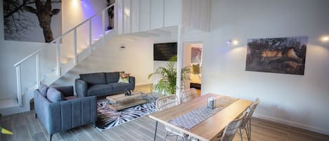 Un salon moderne avec un escalier, des canapés gris, une table à manger en bois et un tapis à motifs zébrés.