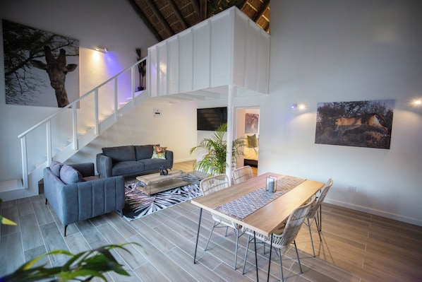 Una sala de estar moderna con una escalera, sofás grises, una mesa de comedor de madera y un tapete estampado de cebra.