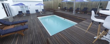Una piscina al aire libre, sombrillas, sillones reclinables de piscina