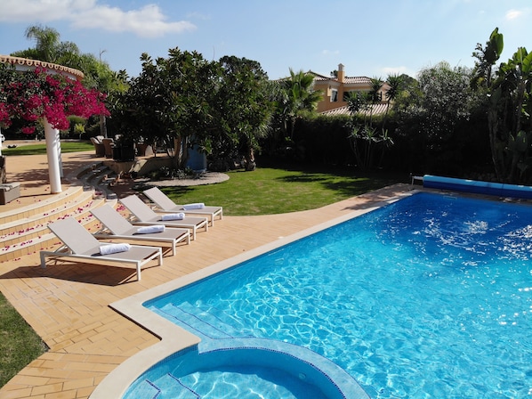 Ein Swimmingpool mit Liegestühlen und einer Pergola mit rosa Blüten.